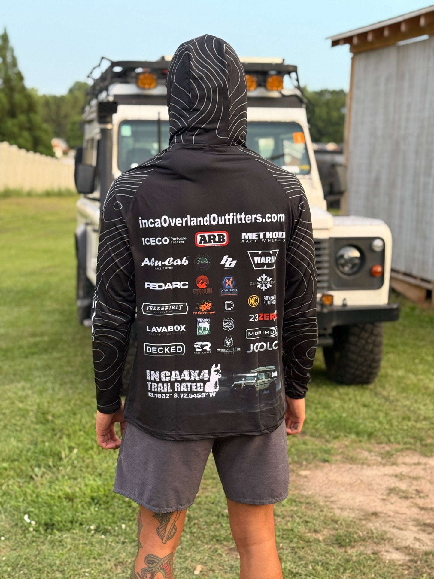 Person wearing a black hoodie with brand logos in front of an off-road vehicle.